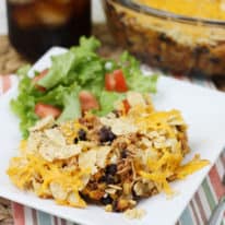Mexican cicken casserole on a white plate with a side salad behind it