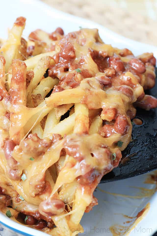 a spatula lifting up french fries topped with chili and melted cheddar cheese