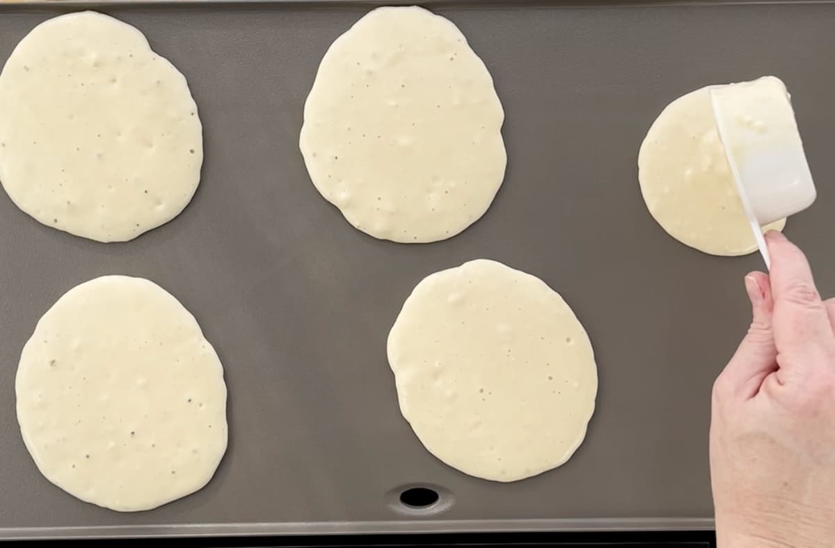 Scooping pancake batter onto a griddle.