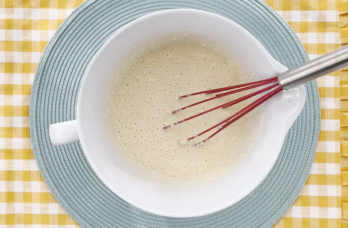 Mixed pancake batter in a white bowl with a red whisk.