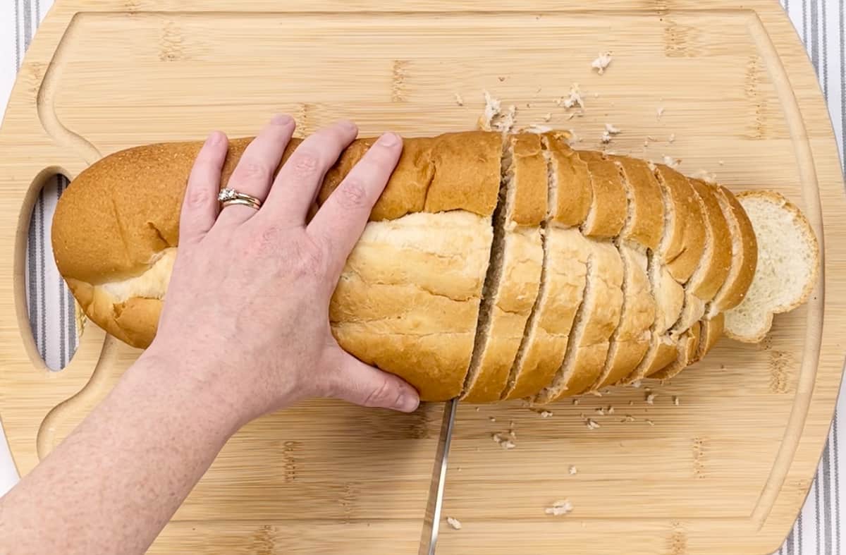Slicing Italian bread on a wood cutting board.