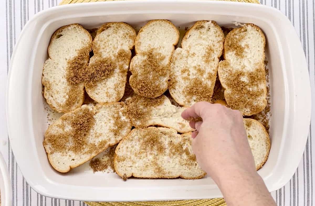 Sprinkling a brown sugar mixture over bread slices in a baking dish.