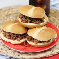 Slow cooker sloppy joes stacked on a red plate with a glass of soda
