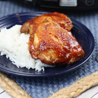 Slow cooker sticky chicken pieces on top of rice on a blue plate
