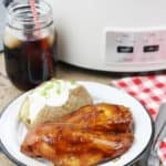 Crockpot BBQ chicken on a white plate with a slow cooker in the background.