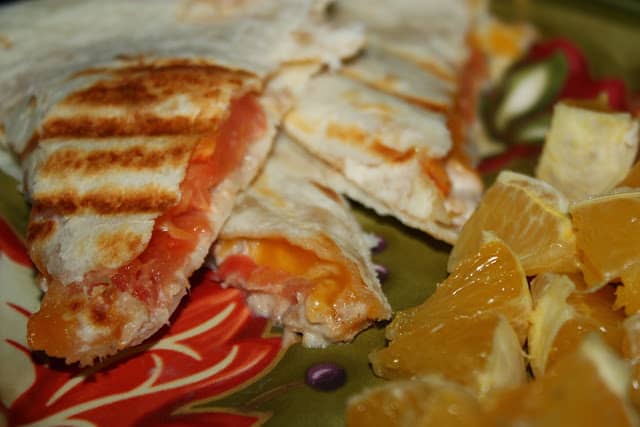 Sliced tuna melt quesadillas next to oranges on a plate.