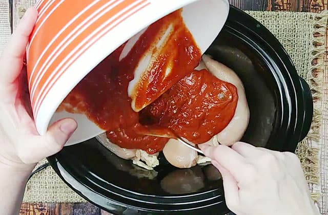 Pouring salsa sauce over chicken breasts in a Crockpot