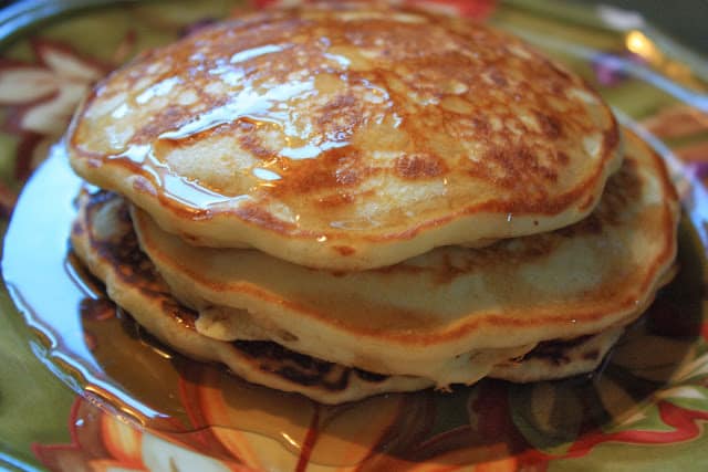 A stack of pancakes on a green plate with syrup on top.