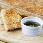 No knead focaccia sliced on a cutting board next to dipping oil.