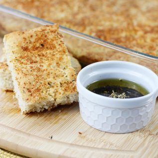 No knead focaccia sliced on a cutting board next to dipping oil.