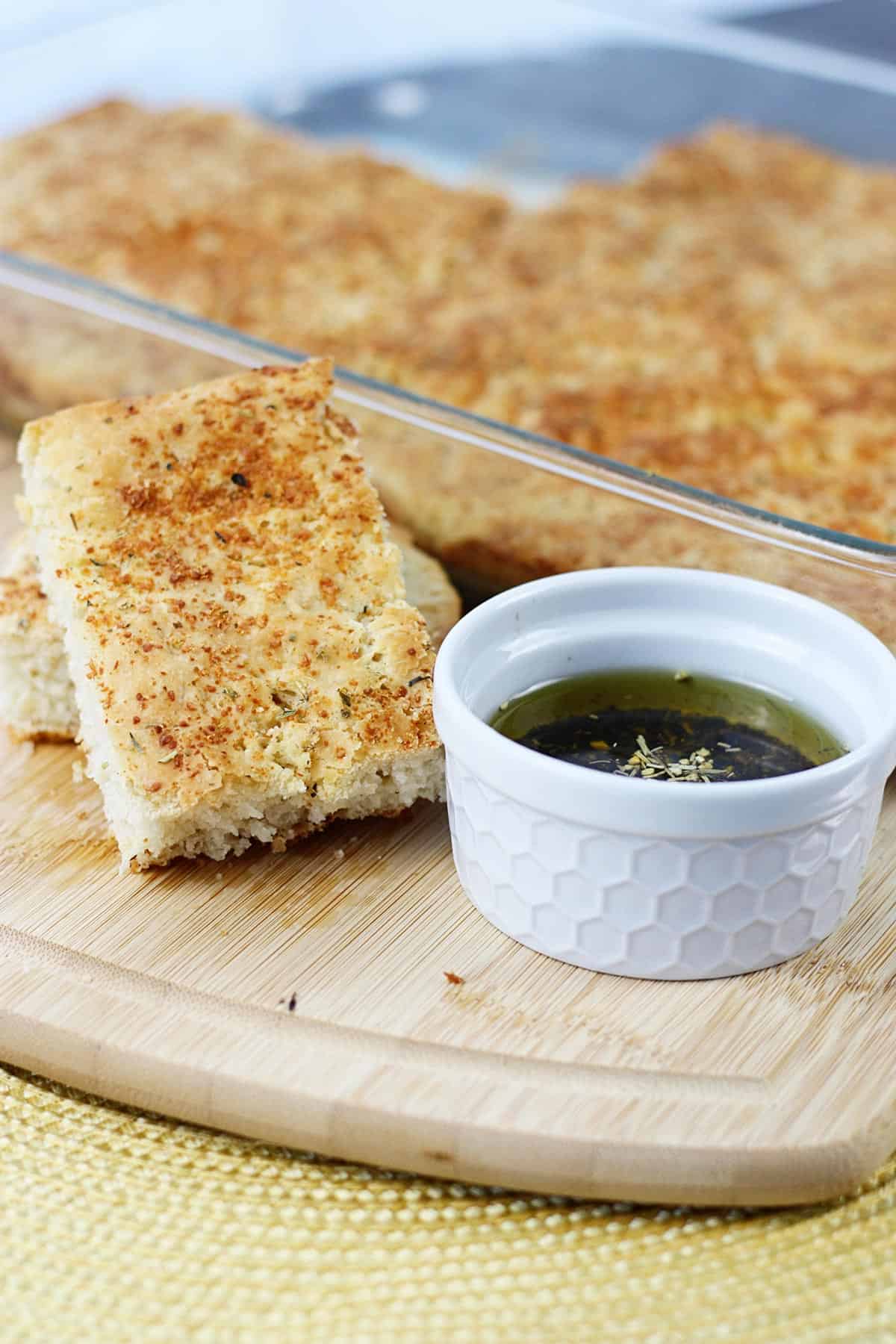 No knead focaccia sliced on a cutting board next to dipping oil.