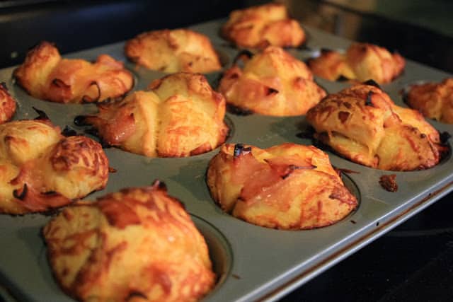Ham and cheese muffins in a muffin tin in the oven.