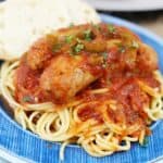 Cooked Italian sausage on a blue plate with spaghetti.