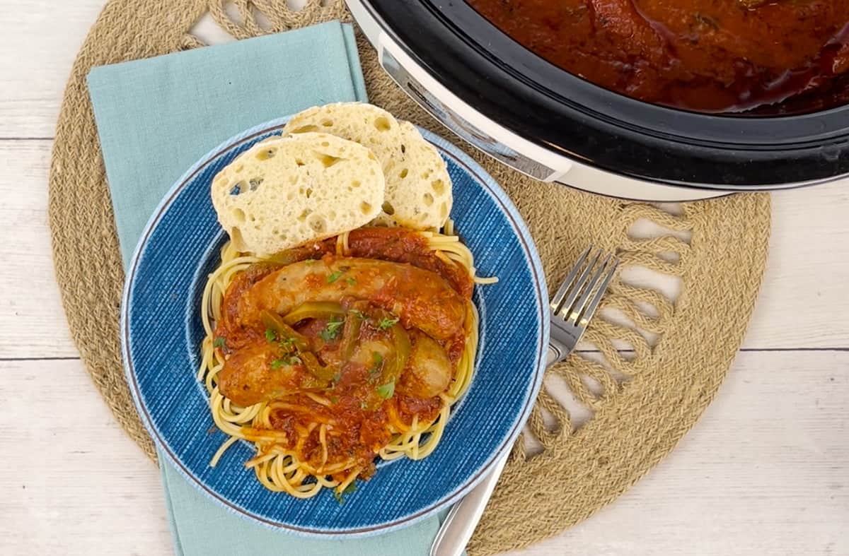 A plate of spaghetti with Italian sausage next to a Crockpot.