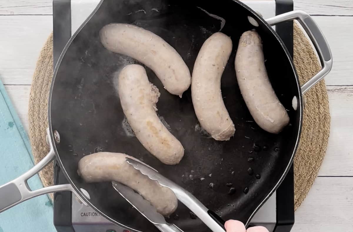 Turning sausage links in a skillet with a pair of metal tongs.