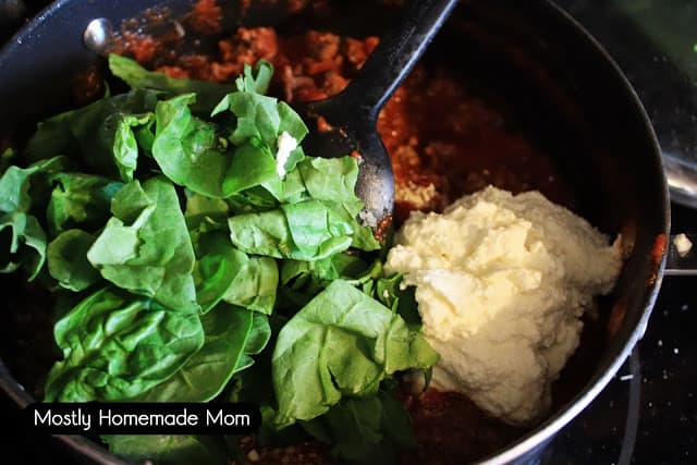 Spinach leaves, ricotta, ground beef, and tomato sauce being mixed in a large skillet.