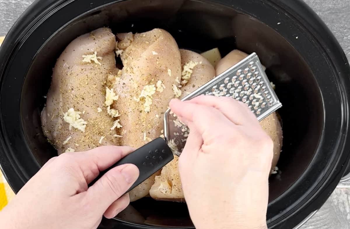 Grating garlic over chicken in a Crockpot.