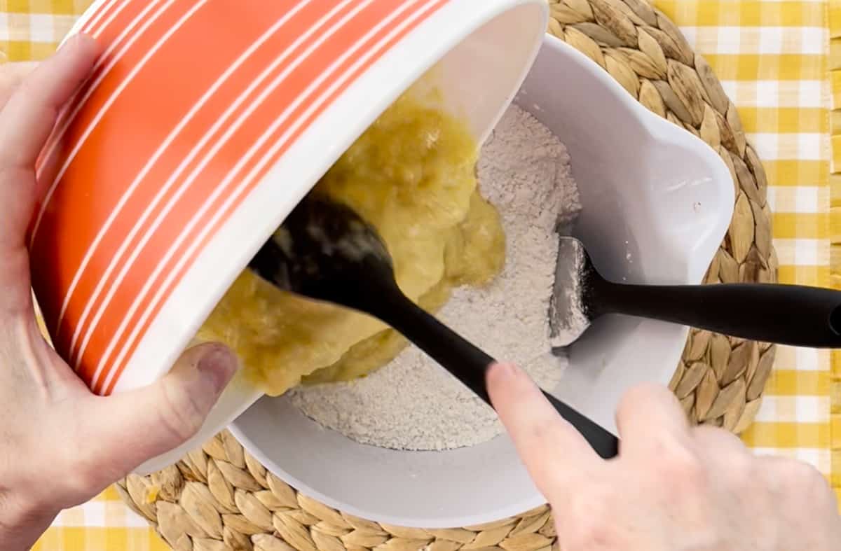 Pouring mashed bananas into the flour in a white mixing bowl.