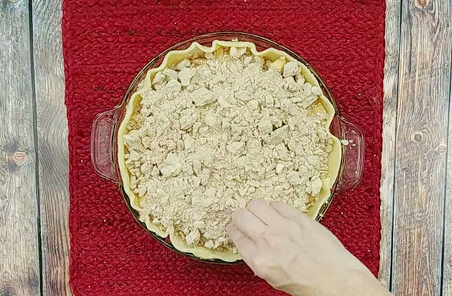 Sprinkling topping over apple crumb pie before baking in the oven