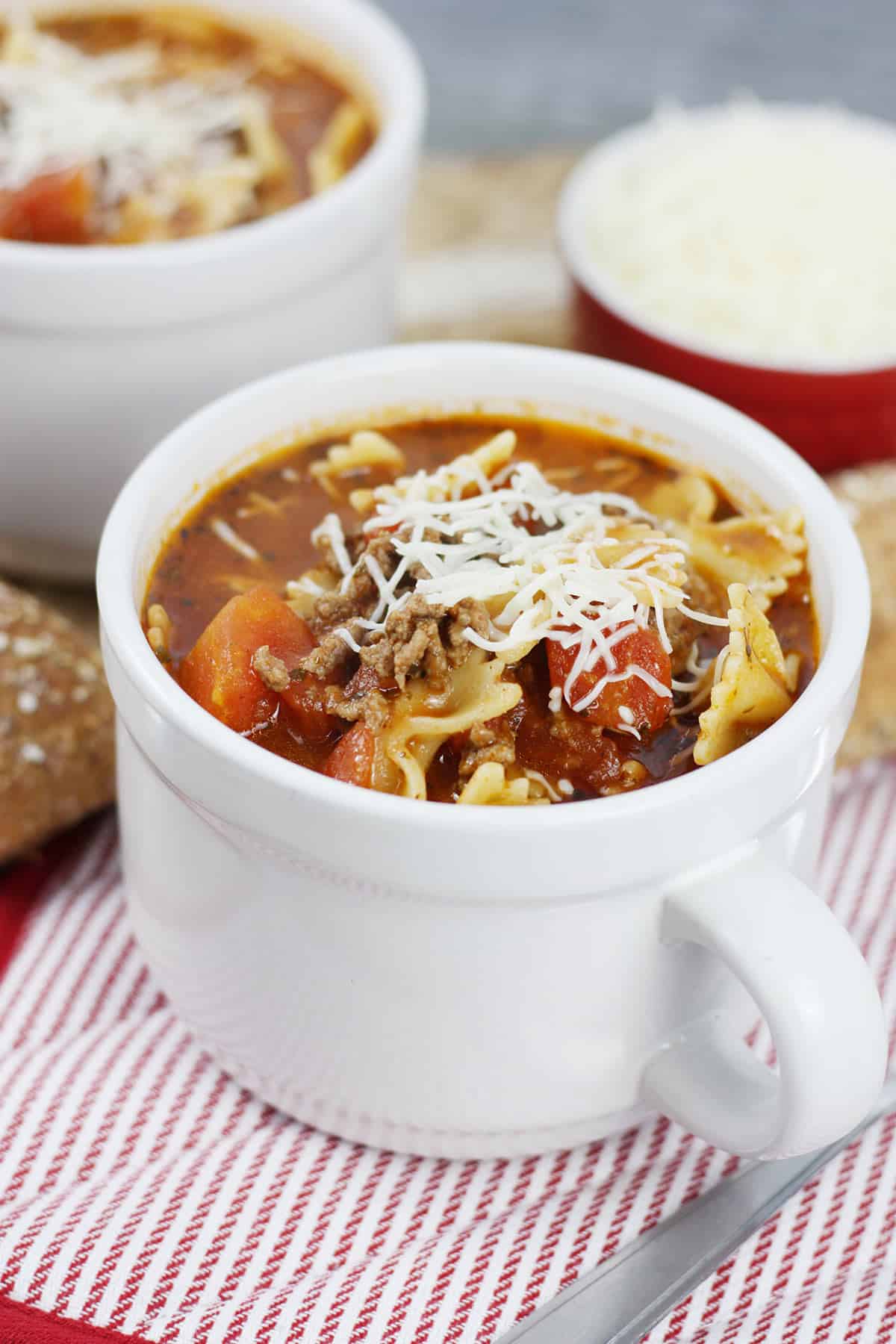 A white soup mug with lasagna soup and shredded cheese.