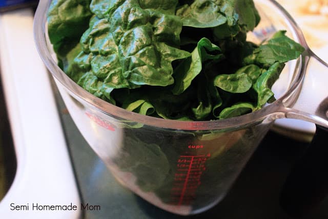 Fresh spinach leaves in a plastic measuring cup.