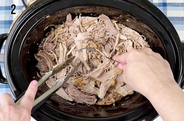 Shredding a pork roast in a slow cooker with a fork and a pair of tongs