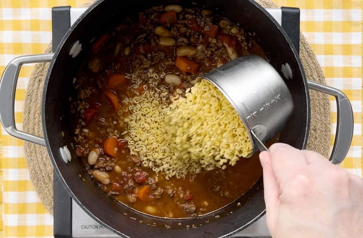 Pouring in alphabet pasta to a soup in a pot.