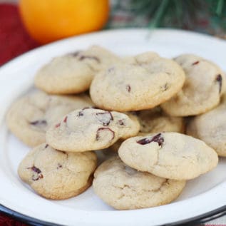 Cranberry orange cookies on a white plate with an orange in the background