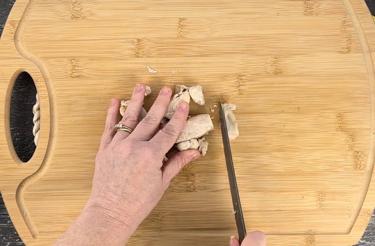Slicing grilled chicken strips on a wood cutting board.