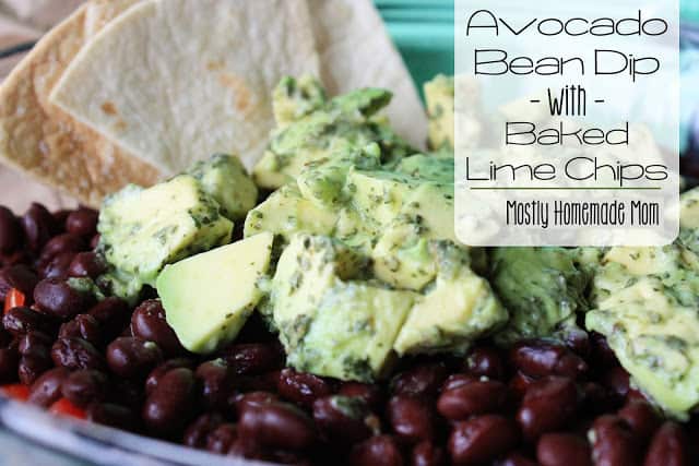 Avocado bean dip with tortilla chips in the background.