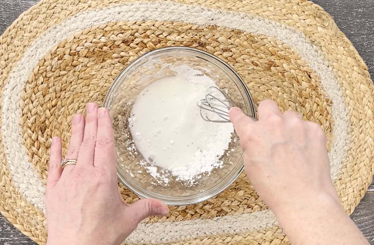 Whisking cornstarch and water in a glass bowl.