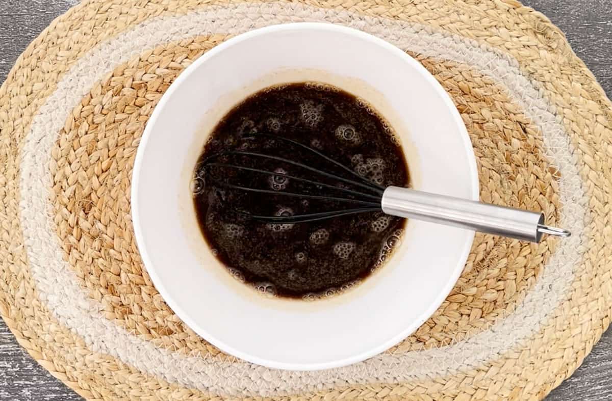 Coca cola sauce and a whisk in a white bowl.