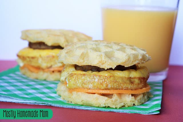 Two waffle breakfast sandwiches with a glass of orange juice.