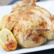 Crockpot BBQ rotisserie chicken on a serving plate next to a lemon