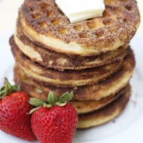 A stack of churro waffles on a white plate with strawberries