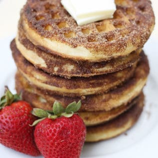 A stack of churro waffles on a white plate with strawberries