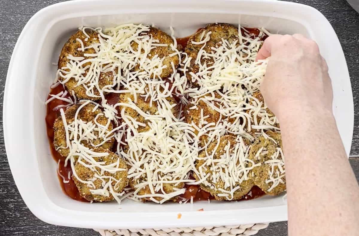 Sprinkling cheese over eggplant in a dish.