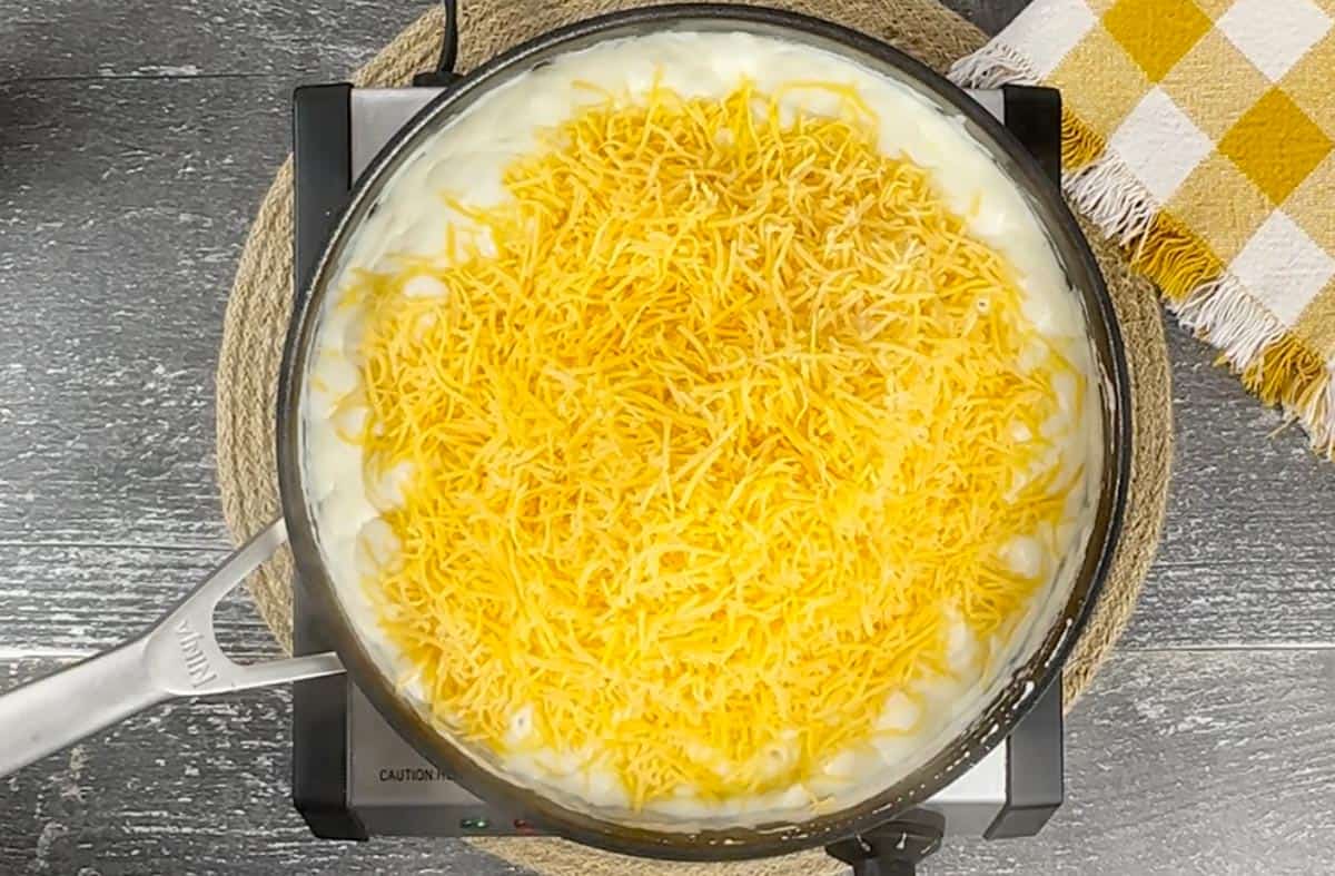 Adding shredded cheddar cheese to the skillet.