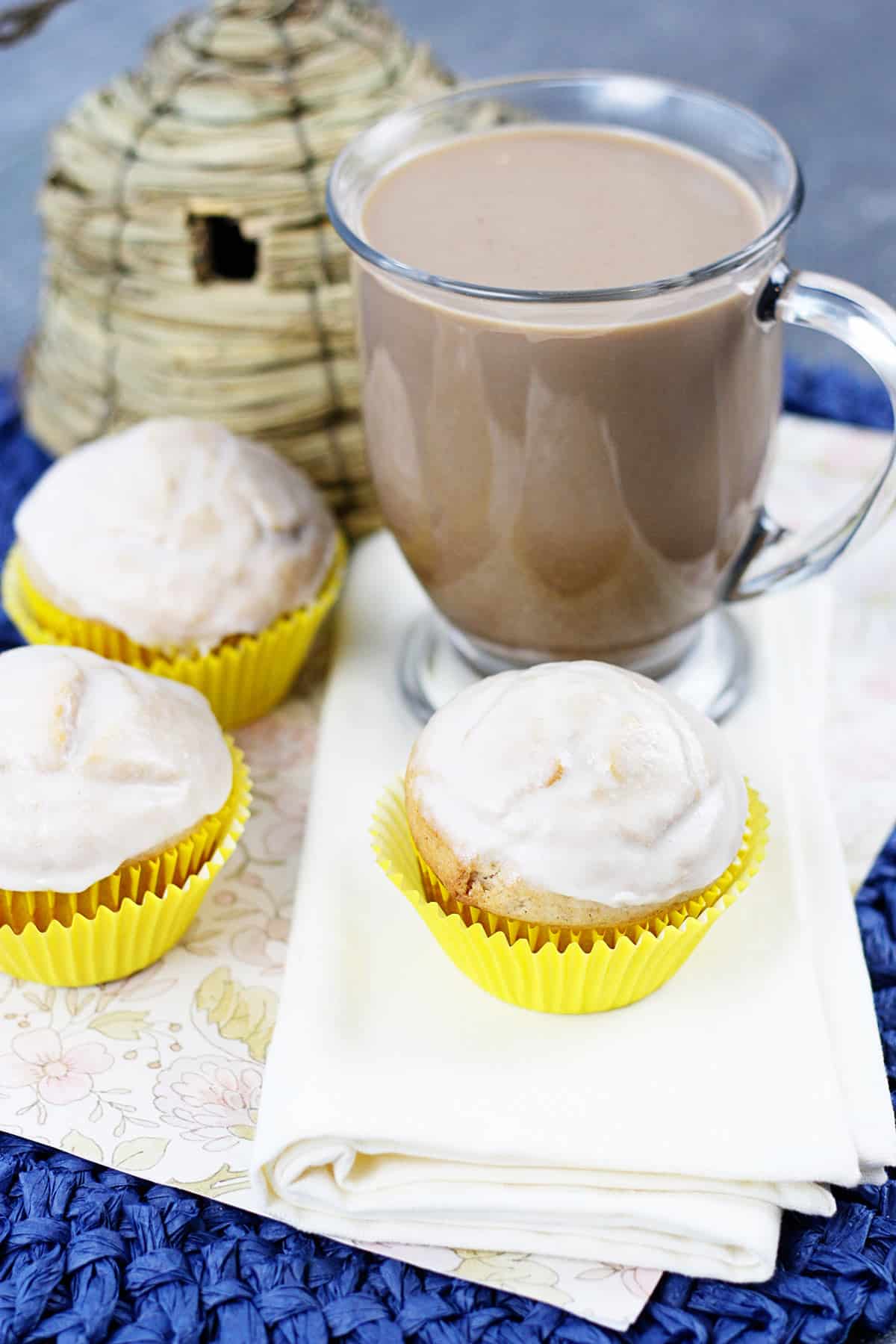 Glazed doughnut muffins on a white napkin with a coffee behind them.