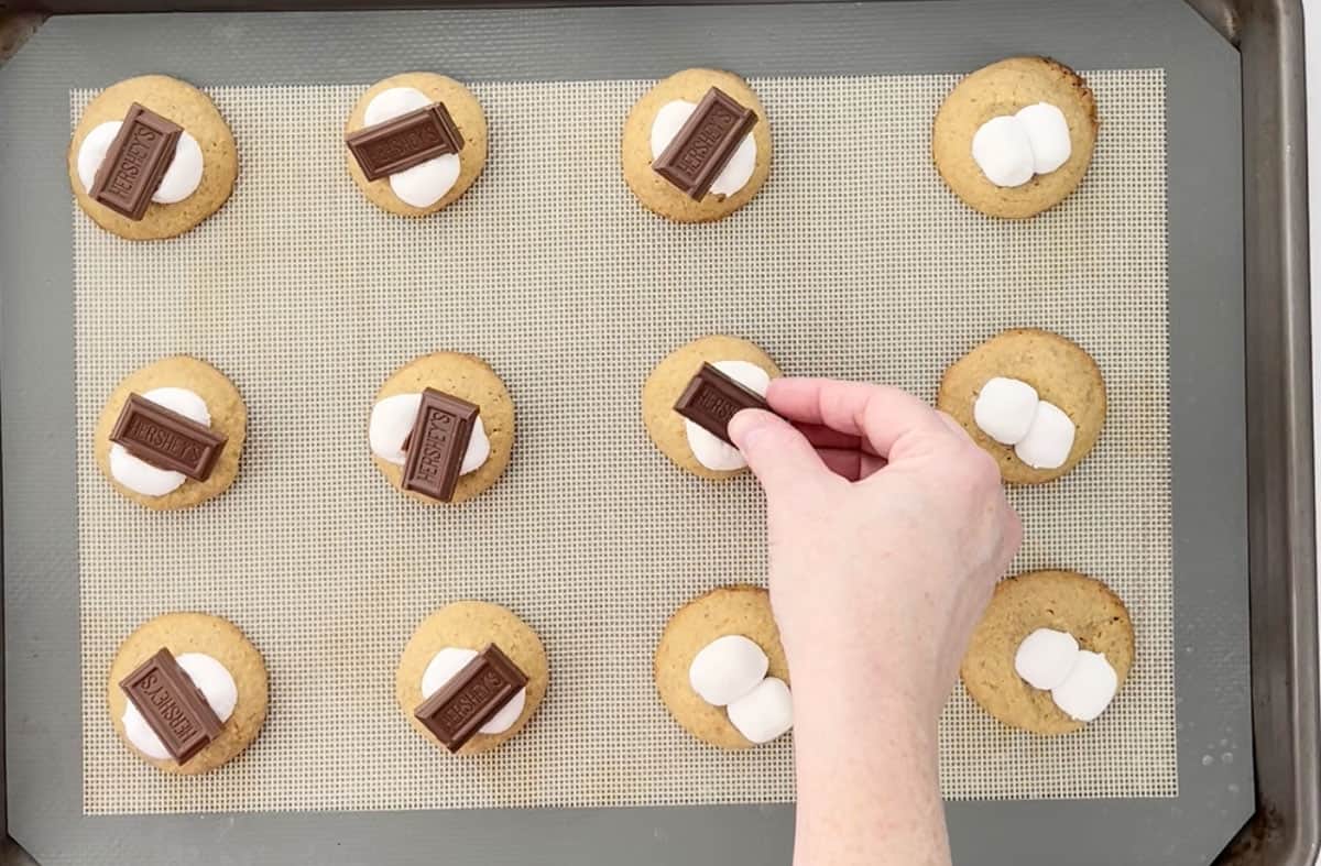 Placing chocolate bars onto cookies on a cookie sheet.