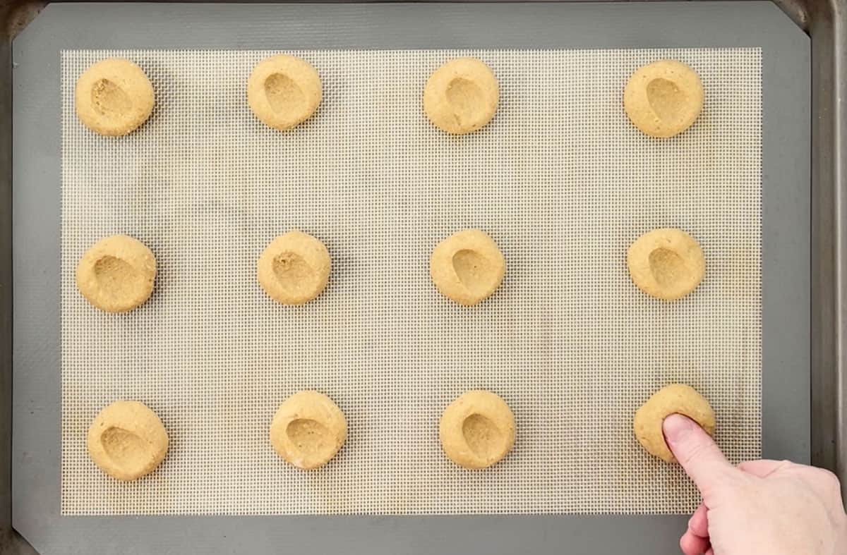 Pressing an indent into cookie dough on a cookie sheet.