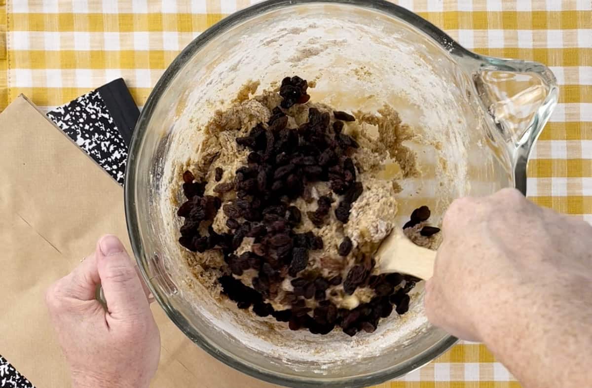 Stirring raisins into the muffin batter in a glass bowl.