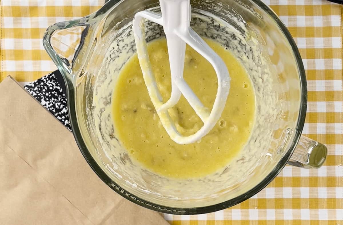 A glass stand mixer bowl with a banana mixture blended.