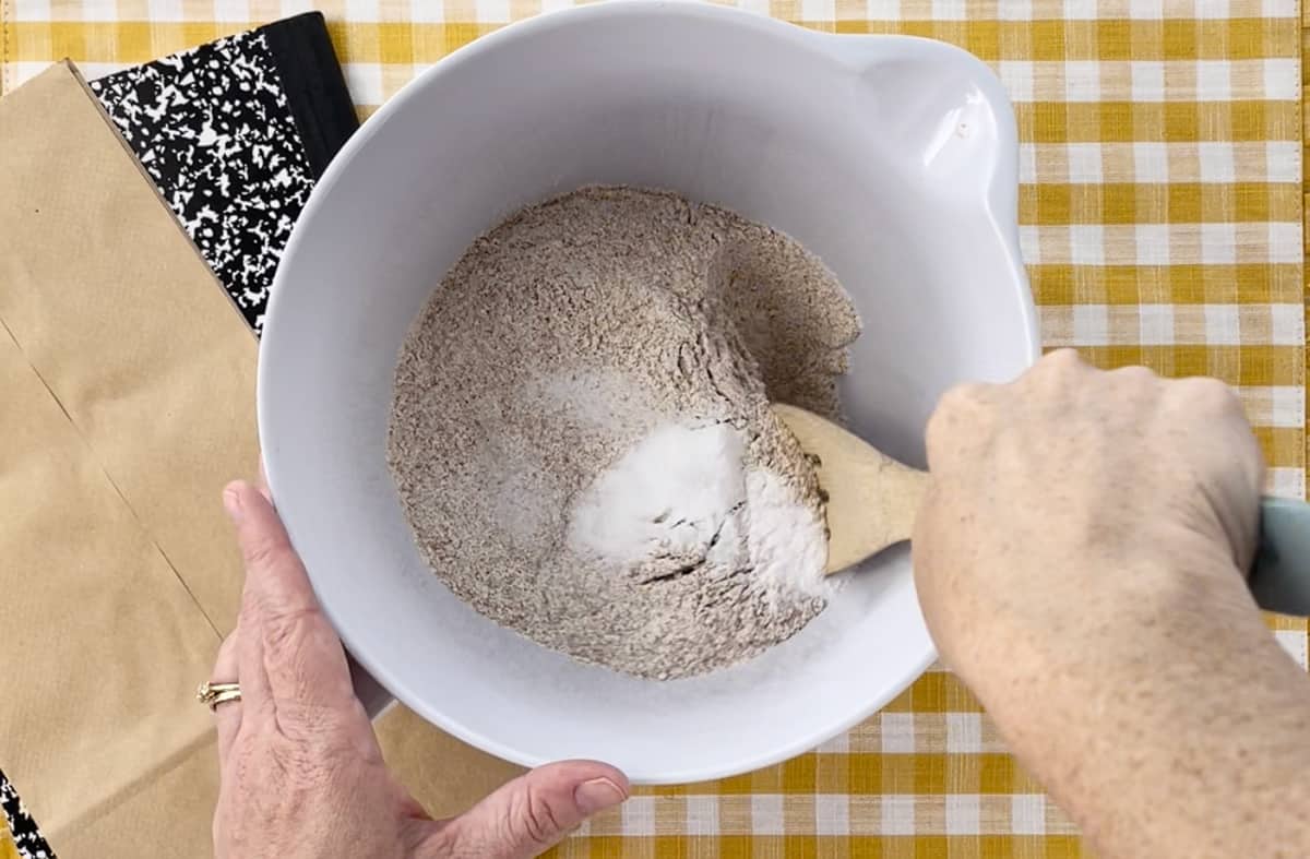 Stirring flour in a white mixing bowl with a wooden spoon.