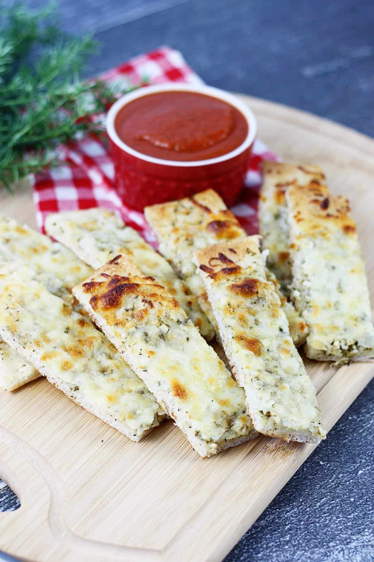 Pizza sticks on a cutting board with pizza sauce.