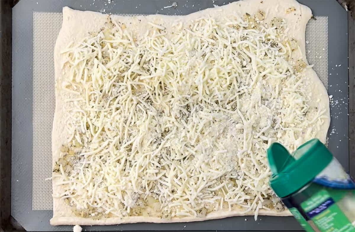 Sprinkling grated Parmesan cheese over the pizza dough on a cookie sheet.