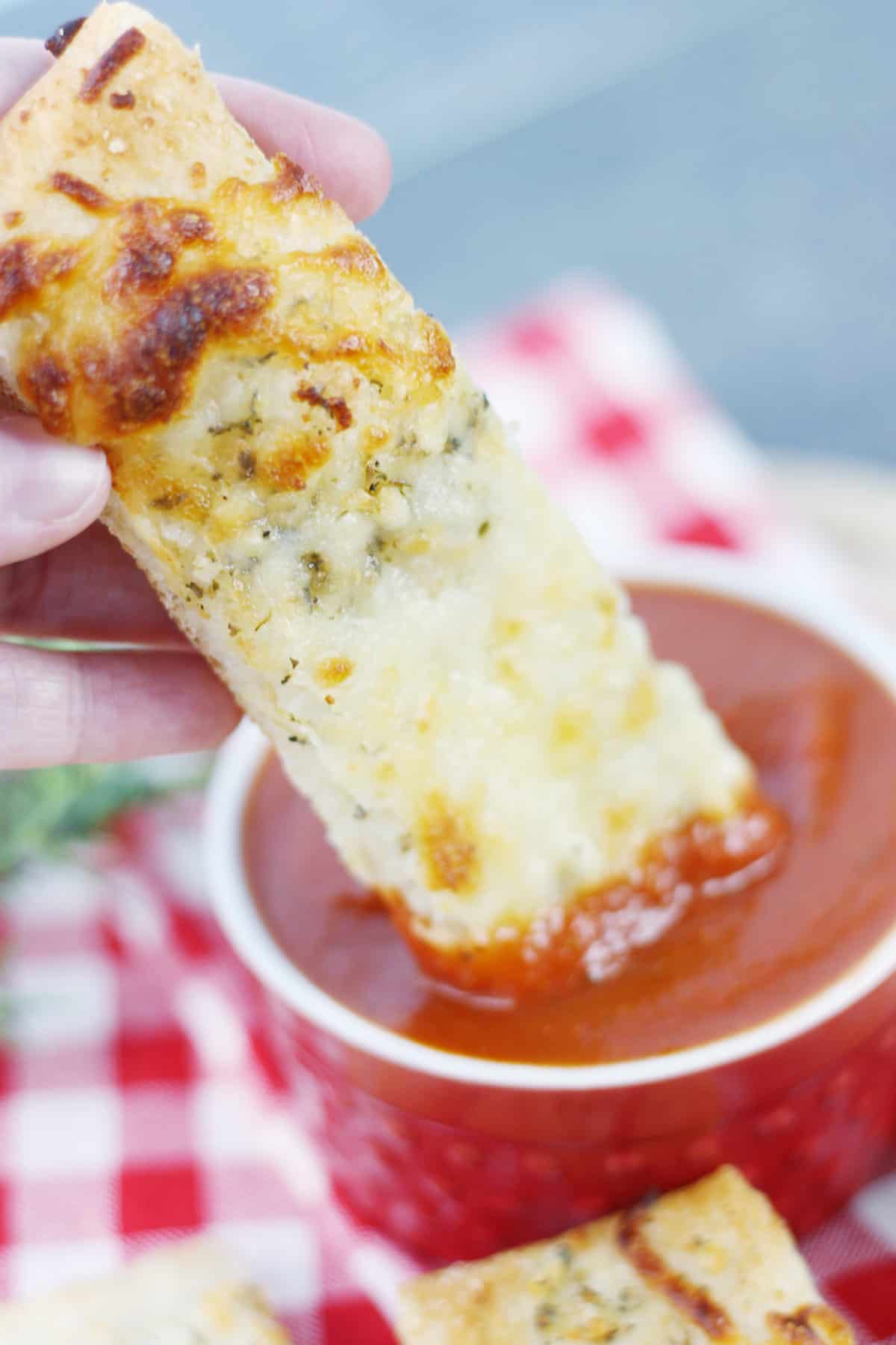 Dipping a pizza stick into some pizza sauce.