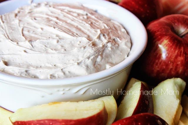 A bowl of cream cheese dip with fruit and apples next to it.