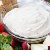 Cream cheese fruit dip in a glass bowl with fruit around it.