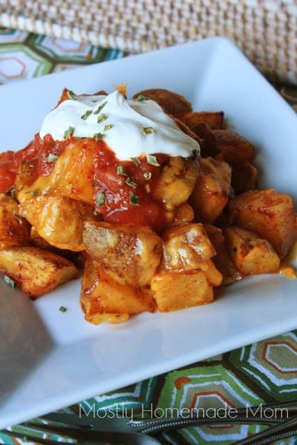 A plate of nacho potatoes with sour cream and salsa.